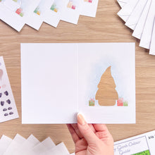 Load image into Gallery viewer, A hand holds an open white greeting card with a small gonk cut-out of the right hand panel on a light wood tabletop. The card is embellished with small colorful gift boxes at the base.