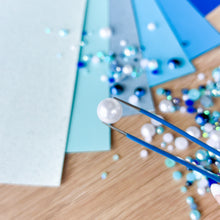 Load image into Gallery viewer, Close up of a blue-white pearl held by tweezers