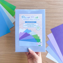 Load image into Gallery viewer, Hand holding a paper pack with colorful papers on a wooden surface