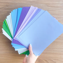 Load image into Gallery viewer, Hand holding a stack of colorful paper sheets on a wooden surface