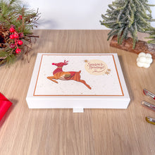 Load image into Gallery viewer, White box with a Christmas design featuring a reindeer and 'Season's Greetings' text on a wooden surface.