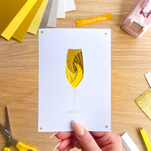 Load image into Gallery viewer, Hand holding a white card with a yellow and gold iris folded paper glass design on a wooden table with craft supplies.