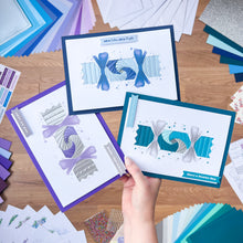 Load image into Gallery viewer, Hand holding three Cracker cards with decorative elements on a wooden surface with various craft materials.