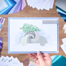 Load image into Gallery viewer, Hand holding a card with an iris fold spiral car design on a wooden surface with craft materials.