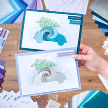 Load image into Gallery viewer, Two car Christmas cards with winter-themed designs on a wooden surface surrounded by craft materials.