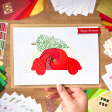 Load image into Gallery viewer, Hand holding a Christmas Car card with red iris fold spiral design on a wooden surface.