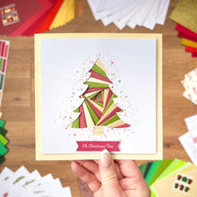 Load image into Gallery viewer, Hand holding a Christmas card with a colorful tree design on a wooden surface.