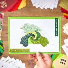 Load image into Gallery viewer, Hand holding a Christmas Car-themed greeting card with an iris fold green spiral design on a wooden surface.