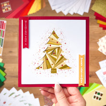 Load image into Gallery viewer, Hand holding a Christmas card with a gold tree design on a wooden surface.