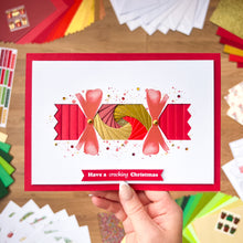 Load image into Gallery viewer, Hand holding a Christmas Cracker card with decorative elements on a wooden surface.