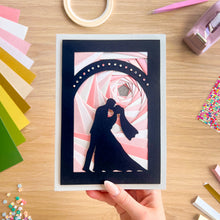 Load image into Gallery viewer, Handmade card with a couple kissing design on a wooden table with craft supplies.