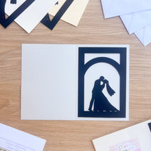 Load image into Gallery viewer, Silver grey card with a cut-out design of a couple kissing on a wooden surface