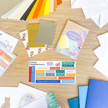 Load image into Gallery viewer, Collection of printed embellishments and card-making supplies on a wooden surface