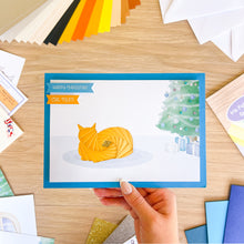 Load image into Gallery viewer, Hand holding a Christmas card with an iris folded cat on a wooden table with craft materials.