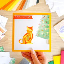 Load image into Gallery viewer, Hand holding a Christmas card with a geometric cat design and festive text.