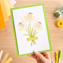 Load image into Gallery viewer, Hand holding a card with iris folding daffodil design and text on a wooden surface with stationery items.