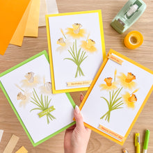 Load image into Gallery viewer, Three greeting cards with floral daffodil designs on a wooden surface with stationery items.