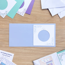 Load image into Gallery viewer, Open card with round design on a wooden surface with other cards and materials.