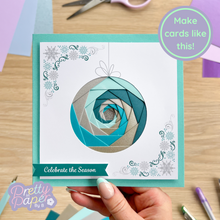 Load image into Gallery viewer, Handmade card with geometric design held by a hand, surrounded by crafting materials on a wooden surface.