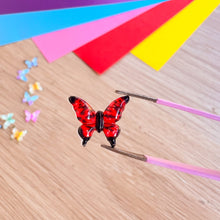 Load image into Gallery viewer, Red butterfly-shaped gem on a wooden surface with colorful paper in the background