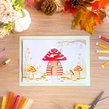 Load image into Gallery viewer, An A4 picture card featuring an iris fold mushroom house, styled in a flat-lay on a wooden desk surrounded by autumn leaves, flowers, coloured paper strips, and scissors.
