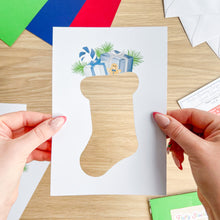 Load image into Gallery viewer, Hand holding a Christmas card with a stocking design on a wooden surface.
