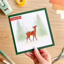 Load image into Gallery viewer, Hand holding a greeting card with a deer illustration on a wooden surface.