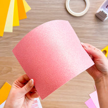 Load image into Gallery viewer, A sheet of pink glitter card bending so the light reflects off it
