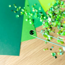 Load image into Gallery viewer, Close-up of green rhinestones being applied with tweezers to green paper.