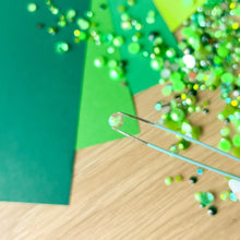Load image into Gallery viewer, Green paper and scattered gems with tweezers in the foreground holding a single gem