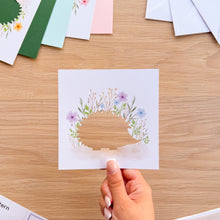 Load image into Gallery viewer, A hedgehog aperture card with blue and lilac printed flowers, set on a light wood tabletop with other colorful cards in the background.
