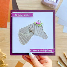 Load image into Gallery viewer, A handmade greeting card held by a hand, featuring a 3D layered horse head design with a pink flower accent. The card has a deep purple border and purple banners that read 'Birthday Wishes' and 'Have a wonderful day'.