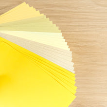 Load image into Gallery viewer, Thirty sheets of A5 paper in 5 different yellow/gold/cream shades on a wooden surface