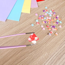 Load image into Gallery viewer, A close-up of a red and white spotted toadstool held by tweezers over a craft table