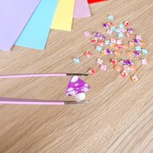 Load image into Gallery viewer, A close-up of a purple and white spotted toadstool held by tweezers over a craft table