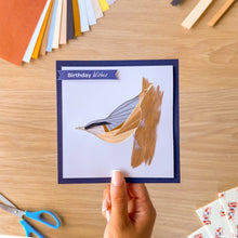 Load image into Gallery viewer, A hand holds a square handmade greeting card featuring an iris fold nuthatch perched on a branch. The card has a navy blue border and a blue banner that reads 'Birthday Wishes'.