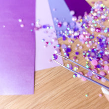 Load image into Gallery viewer, Purple paper with scattered gems on a wooden surface and tweezers holding a single gem