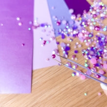 Load image into Gallery viewer, Purple paper with scattered gems on a wooden surface and tweezers holding a single gem