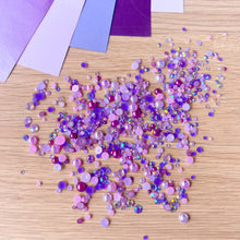 Load image into Gallery viewer, Purple pearl gems scattered on a wooden surface with purple paper in the background.
