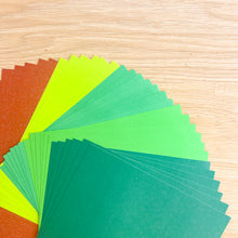 Load image into Gallery viewer, A close-up of a fanned stack of textured paper sheets in multiple shades of green and brown arranged on a light wood surface.
