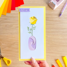 Load image into Gallery viewer, Greeting card with a yellow rose design held by a hand on a wooden surface.