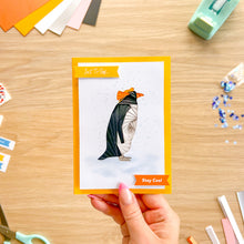 Load image into Gallery viewer, A hand holds a greeting card featuring a stylized penguin with orange head-feathers, with the phrases 'Just To Say' and 'Stay Cool'.
