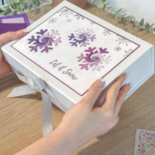 Load image into Gallery viewer, White gift box with snowflake design and 'Let it Snow' text, held by a hand on a wooden surface.