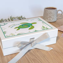 Load image into Gallery viewer, Gift box with turtle design and ribbon on a wooden surface with a mug in the background