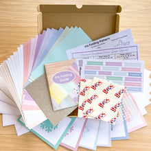 Load image into Gallery viewer, An open cardboard box filled with a variety of pastel-colored paper sheets, patterned cards, stickers, and folding guides, arranged on a light wood surface. Visible text includes 'Iris Folding Guide' and 'Iris Folding Pattern'.