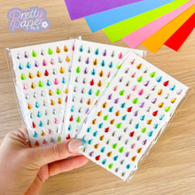 Load image into Gallery viewer, Colorful teardrop gem stickers held by a hand with colorful paper strips in the background.