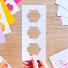 Load image into Gallery viewer, Hand holding a sheet of flower-shaped cut-outs on a wooden table with colourful card in the background.