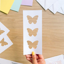 Load image into Gallery viewer, Butterfly cutouts on a card with a hand holding it, on a wooden surface.