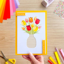 Load image into Gallery viewer, Hand holding a card with a colorful tulip design on a wooden table with craft supplies.