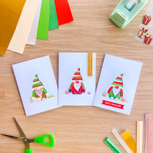 Load image into Gallery viewer, Three handmade greeting cards featuring cute iris fold gonks are arranged on a light wood tabletop with craft supplies like colored paper, scissors, tape, and a punch around them.
